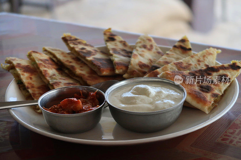 印度自助早餐，撒上焦糖洋葱的aloo parathas切片，白色盘子，填满garam masala土豆的可口面包，酒店餐厅自制aloo paratha菜，raita凝乳酸奶